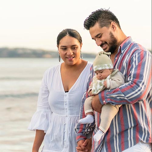 A couple smiling and looking at their newborn baby while walking on a beach