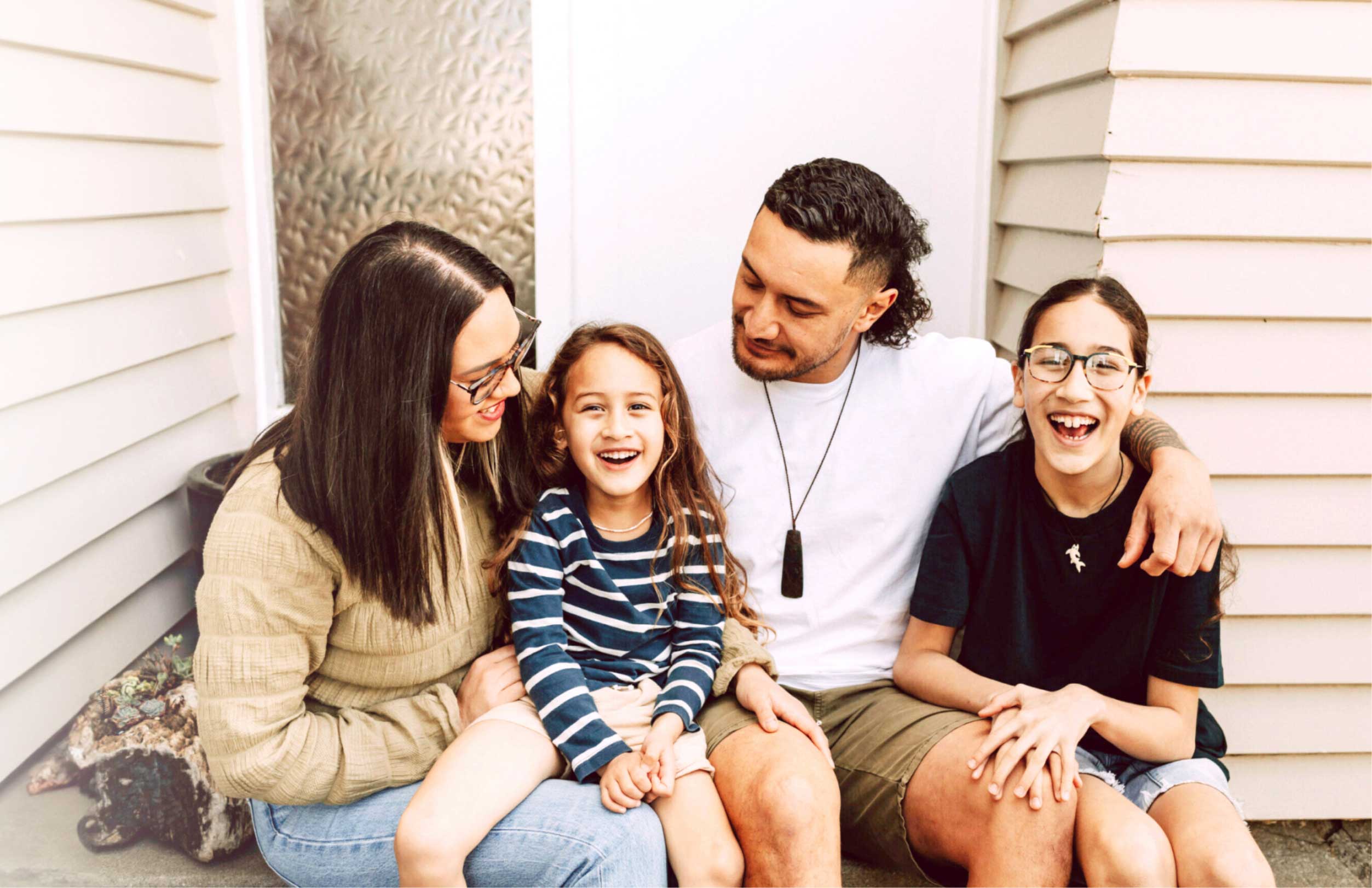 A family of four laughing together on their front porch steps, including two parents and two children
