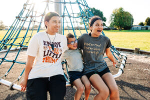 Three kids sitting together on outdoor playground equipment, smiling and laughing