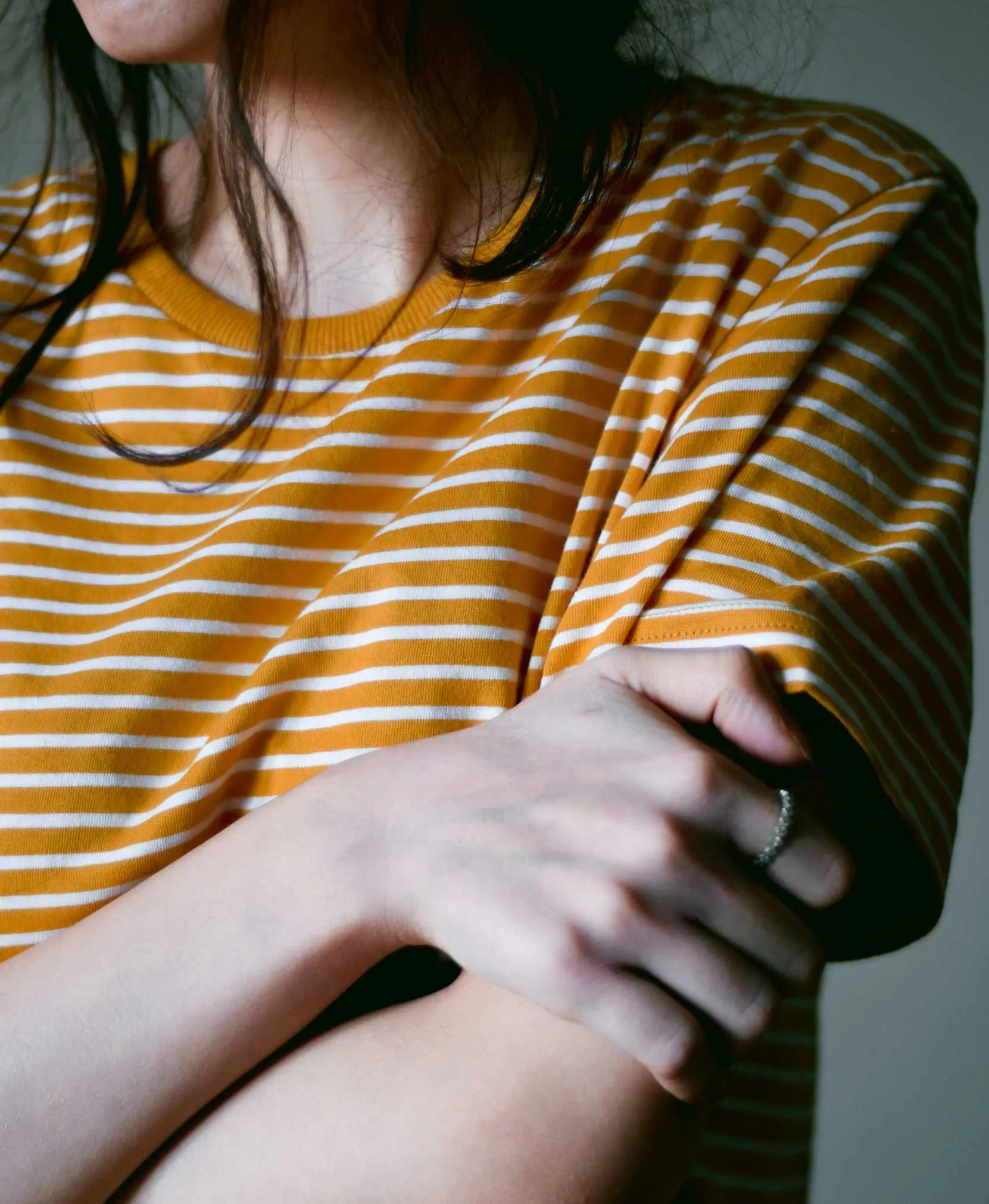 Woman wearing a mustard yellow and white striped crew-neck t-shirt, arms crossed, with a ring on her finger
