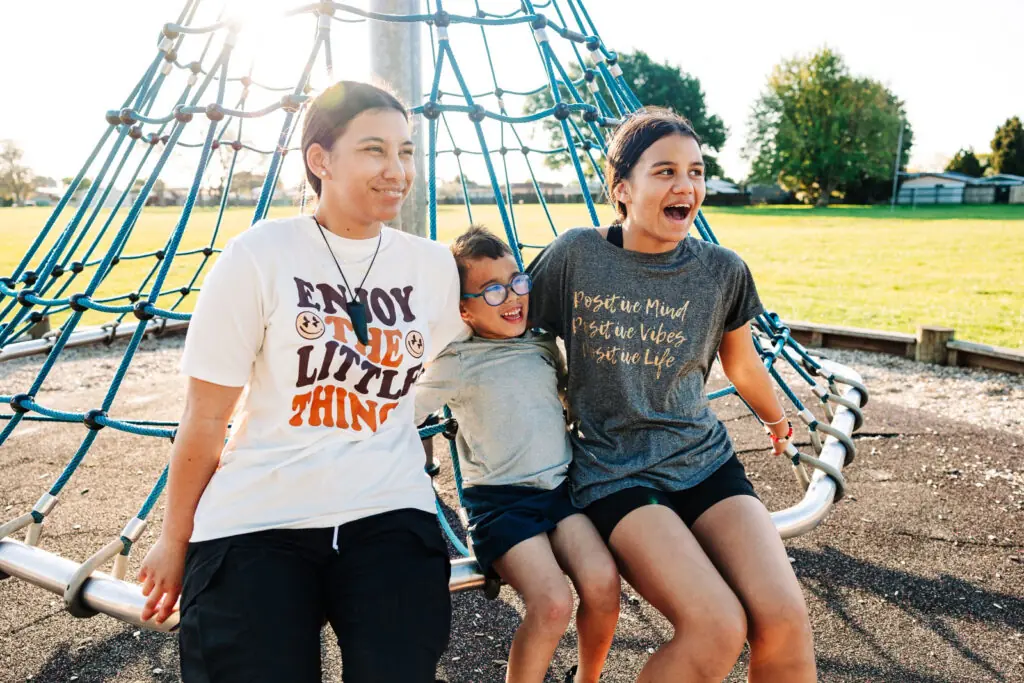 Three kids sitting together on outdoor playground equipment, smiling and laughing