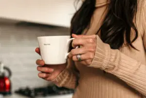 Close-up of hands cradling a white cup of coffee, person wearing a knit sweater